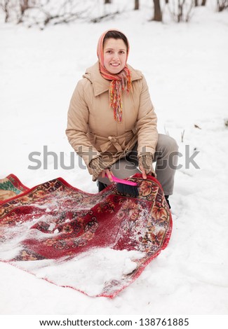 Russian woman cleans carpet with snow in winter day outdoor