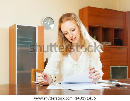 serious blonde woman looking financial documents at table in home