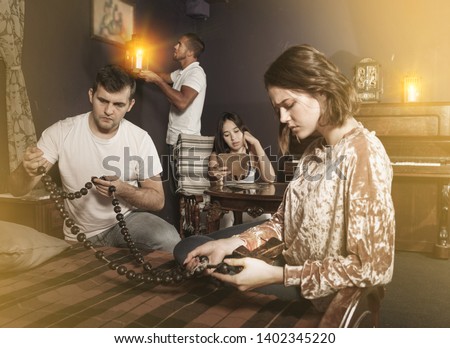 Group of young adults inspecting wooden rosary, trying to find solution of conundrum in escape room with antique furnitures Foto stock © 