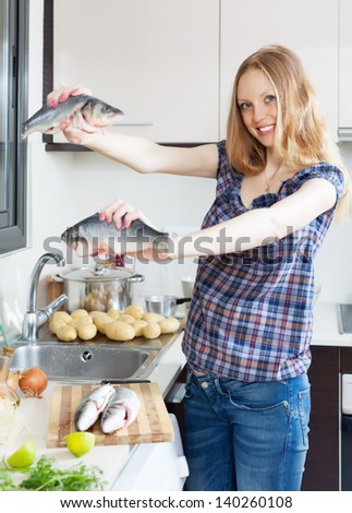 Smiling blonde woman with seabass fish  in domestic kitchen