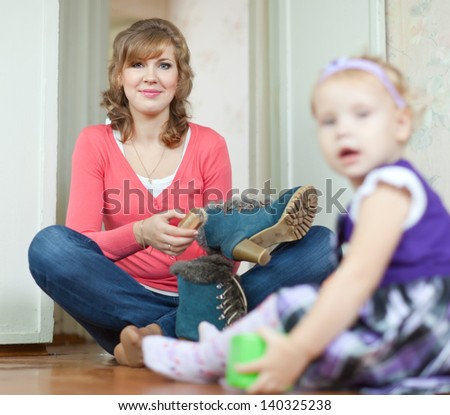 Woman with baby girl sits on floor and cleans shoes