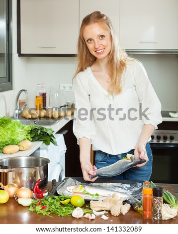 Cheeful woman cooking fish with lemon in sheet pan