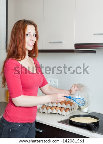 Smiling woman making scrambled eggs in frying pan at home