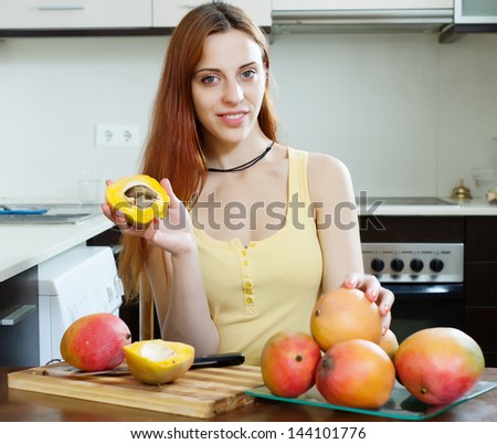 Smiling long-haired woman eating mango at home kitchen