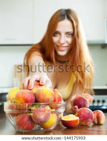long-haired girl taking peaches at home kitchen. Focus on woman