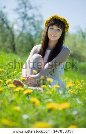 Happy girl sitting outdoor in dandelion meadow
