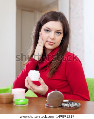 Beautiful woman uses cosmetic cream in home interior