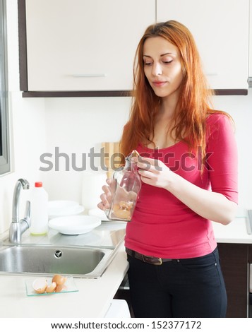 Girl washing glass bottle with egg shell in home kitchen
