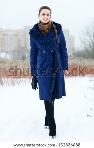 Full length portrait of smiling girl in blue coat at wintry park