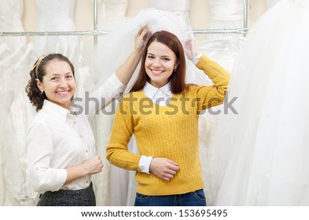 Shop assistant  helps the bride in choosing bridal veil at wedding store