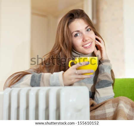 smiling woman  with yellow cup near oil heater at home