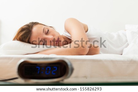 Beautiful sleeping girl in bad with alarm clock in the morning