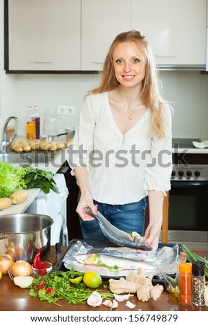Cheeful woman cooking fish with lemon in sheet pan at  kitchen