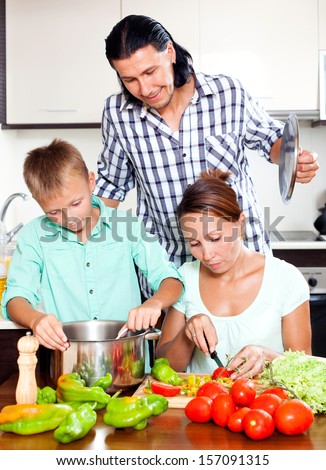 Happy family of three cooking veggie lunch together in home kitchen