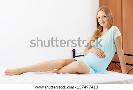 pregnancy girl in nightshirt sitting on white sheet in bed at home