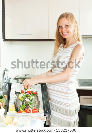Happy woman putting  saltwater fish into sheet pan at kitchen table