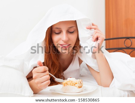 woman eating sweet cake under white sheet in bed