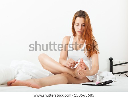 Beautiful young woman cares for toenails with nail lacquer on bad at home