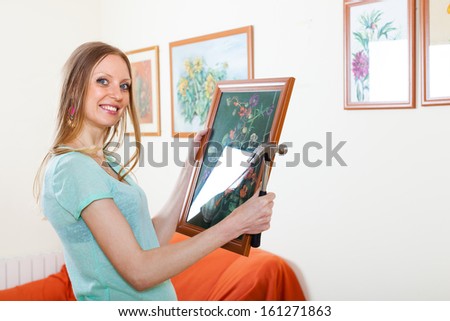 Positive blonde woman hanging the art pictures on wall