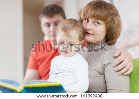 Happy parents with child looks the book in home interior