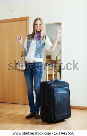 Smiling woman with suitcase near door at home