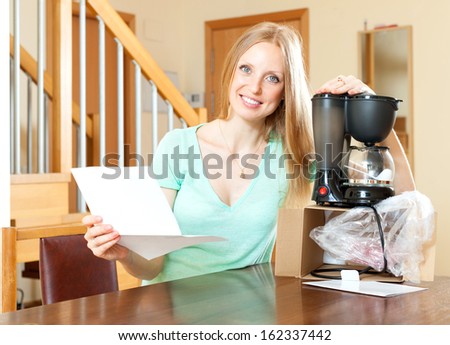 Happy woman reading  warranty card for new coffee machine  at home interior