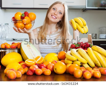 Positive blonde long-haired woman with bananas and other fruits in home kitchen