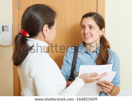 mature woman answer questions of smiling woman with papers at door in home
