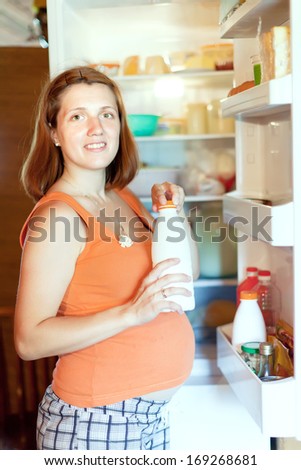 pregnant woman  with milk bottle near refrigerator  at home
