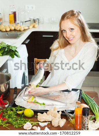Happy woman cooking fish with lemon in sheet pan at home kitchen