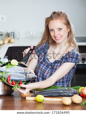 Smiling girl with raw seabass fish in frying pan at home kitchen