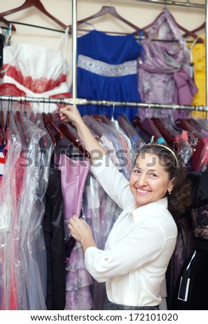 Happy mature woman chooses evening dress at boutique