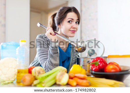 beautiful young woman tests food with ladle in the kitchen