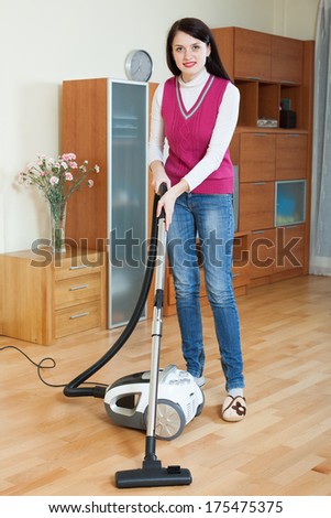 Smiling brunette woman cleaning with vacuum cleaner  at home