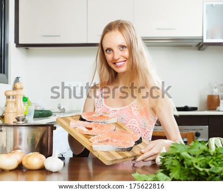 Smiling woman with raw salmon fish  in  kitchen