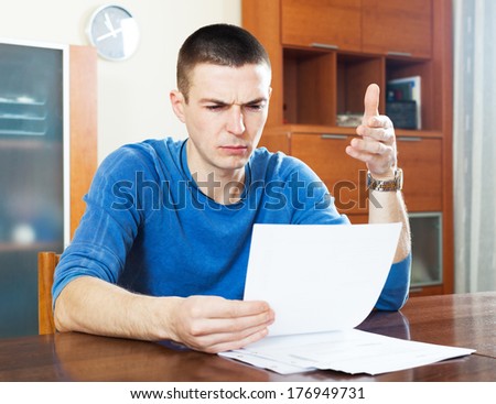Sad frustrated man looking at piece of paper sitting at the table