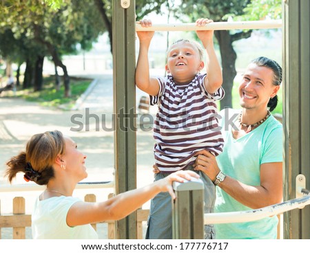 Happy parents with child  training with pull-up bar at playground