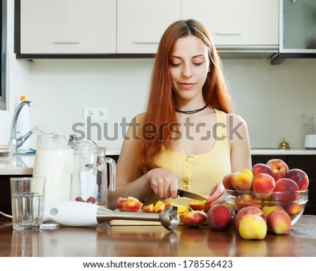 long-haired girl in yellow cooking milk shake with peaches at home kitchen