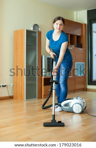 Woman cleans with vacuum cleaner on parquet floor at home