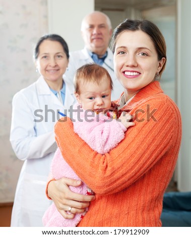 Portrait of happy woman holding baby with doctors in background