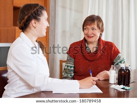 friendly doctor examining mature woman at table in home. Focus on doctor