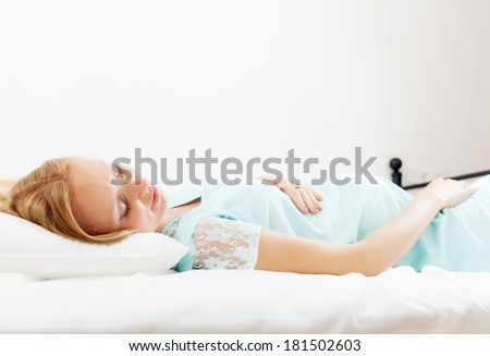 Blonde pregnant woman sleeping on white pillow in bed at home