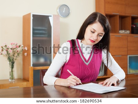 serious woman filling in financial documents at table in home interior