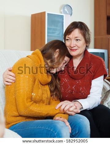 Mature mother comforting crying adult daughter in home