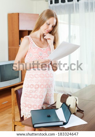 serious pregnant woman reading paper document in home