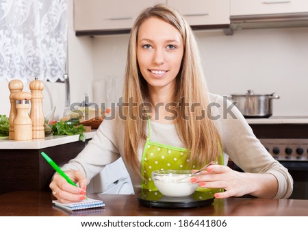 Happy woman weighing curd cheese on kitchen scales