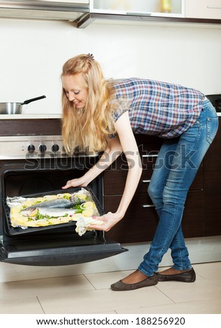 housewife cooking fish and potatoes on sheet pan in oven at home