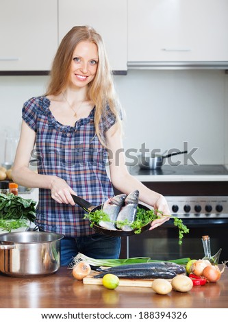 Smiling girl with  seabass fish in fryingpan at home kitchen
