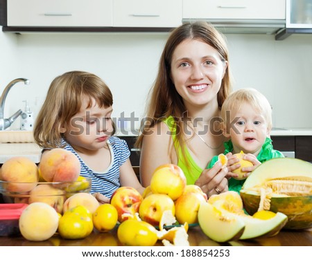 Happy mother with children eating melon and other fruits over  table at home
