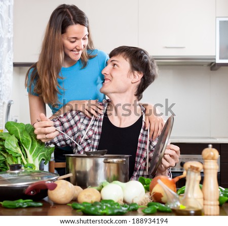 man suggests to try the cooked food to the girl in house kitchen
